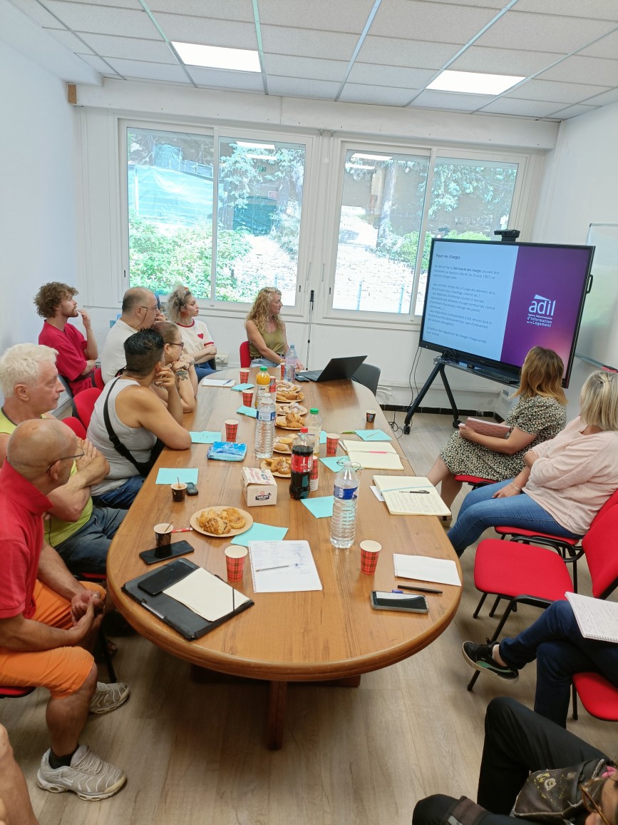 Photographie d'une rencontre organisée autour d'une table ovale, les personnes présentes regardent le support de formation et écoutent les commentaires de la formatrice